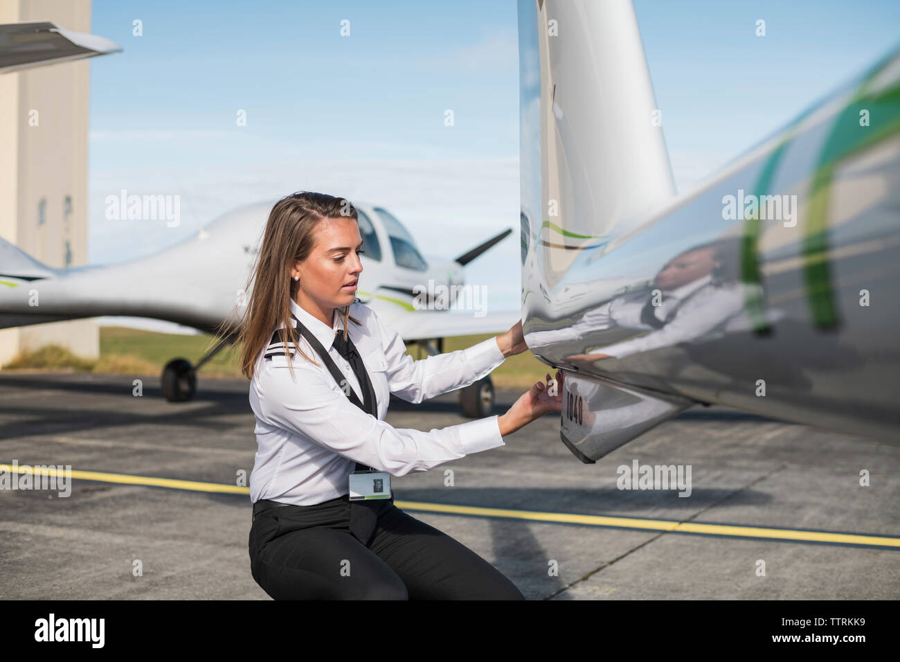 Ingenieurin Prüfung Flugzeug Teile während kauert auf der Piste des Flughafens gegen Himmel während der sonnigen Tag Stockfoto