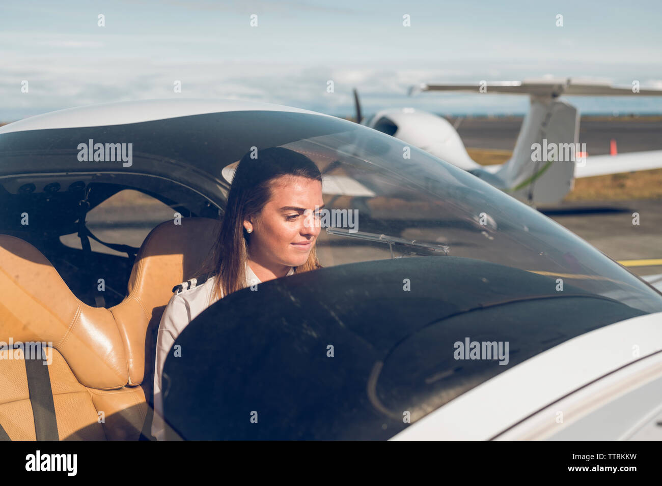 Zuversichtlich weiblichen Piloten im Flugzeug durch die Windschutzscheibe am Flughafen während der sonnigen Tag gesehen sitzen Stockfoto