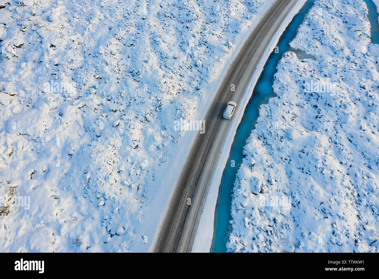 Drone Blick auf Auto fahren auf der Route in der Nähe von Amazing blue water von schmalen Fluss, zwischen Schnee landet im Winter Stockfoto