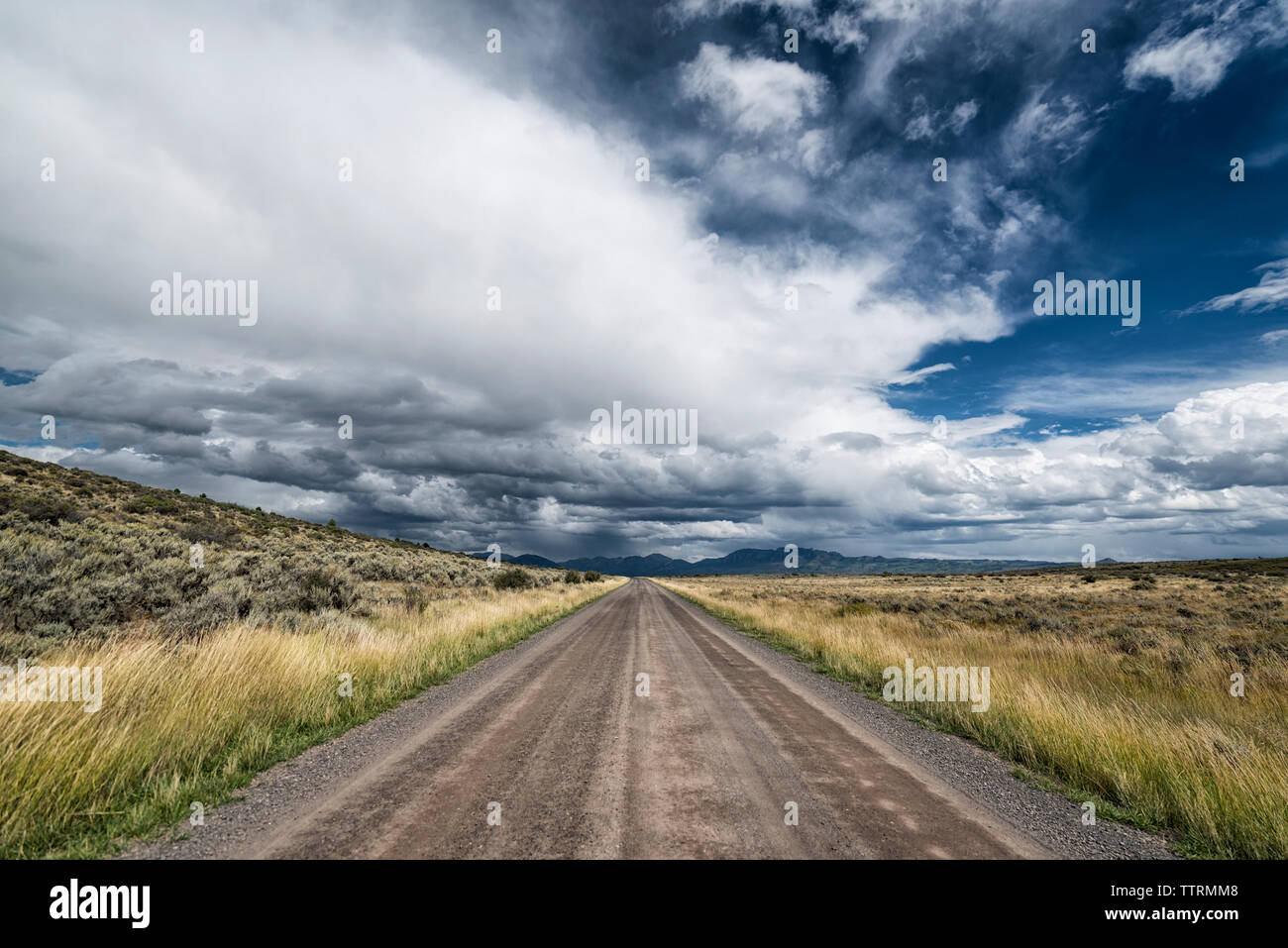 Leere Straße inmitten von Feld gegen bewölkter Himmel Stockfoto