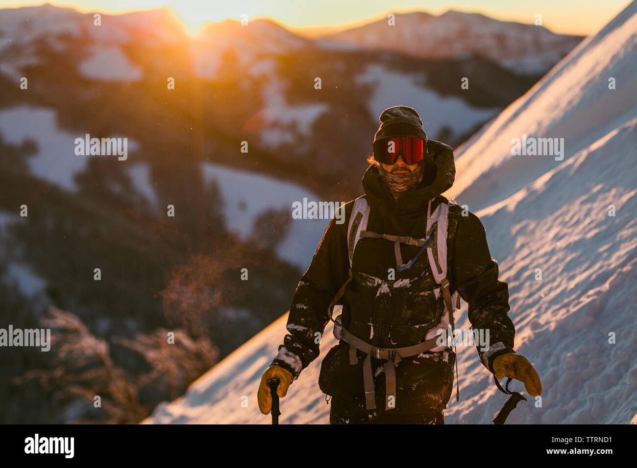 Mann in Ski-wear stehen auf schneebedeckte Berge bei Sonnenuntergang Stockfoto