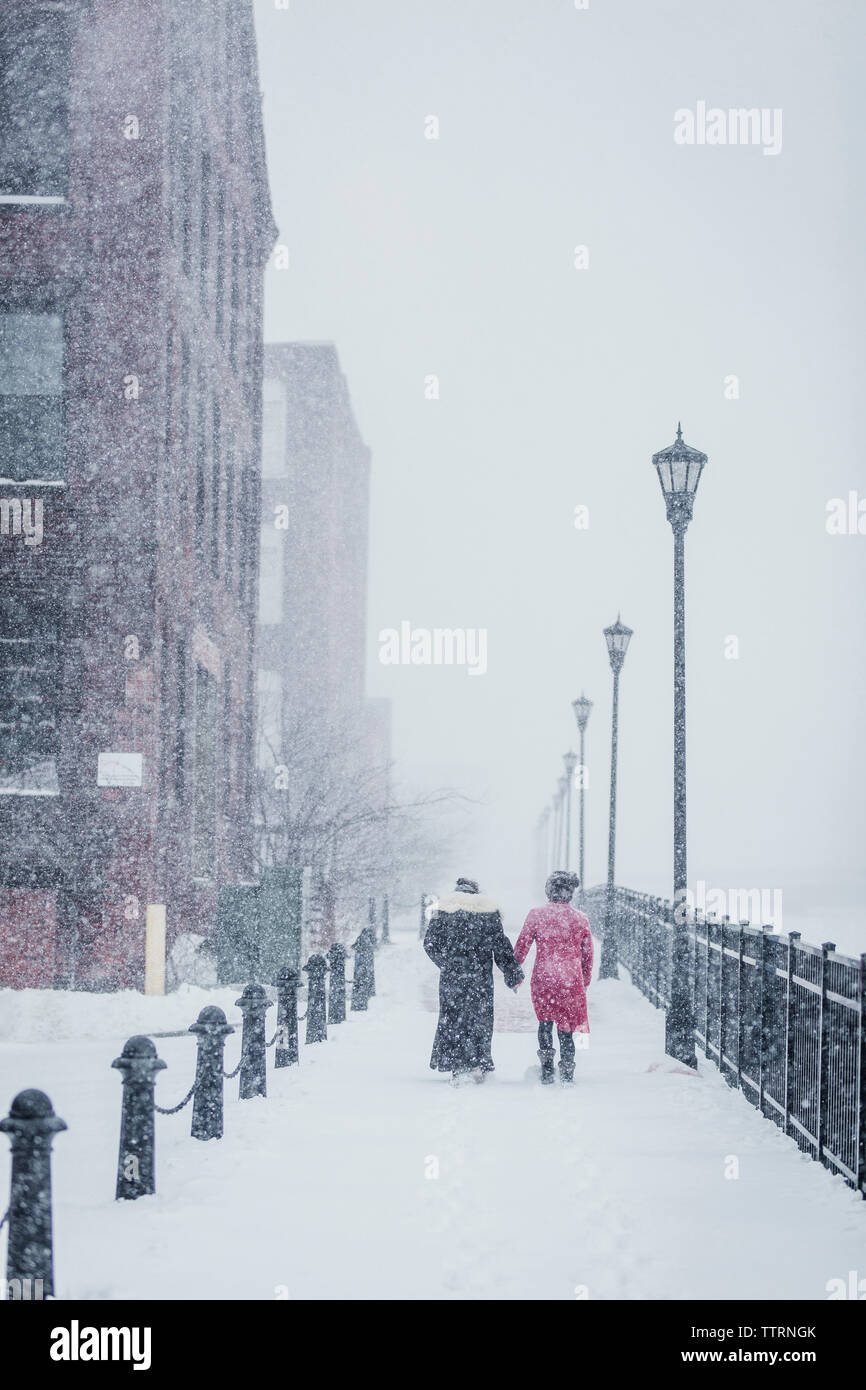 Ansicht der Rückseite des weiblichen Freunden Wandern inmitten Geländer in der Stadt bei Schneefall Stockfoto