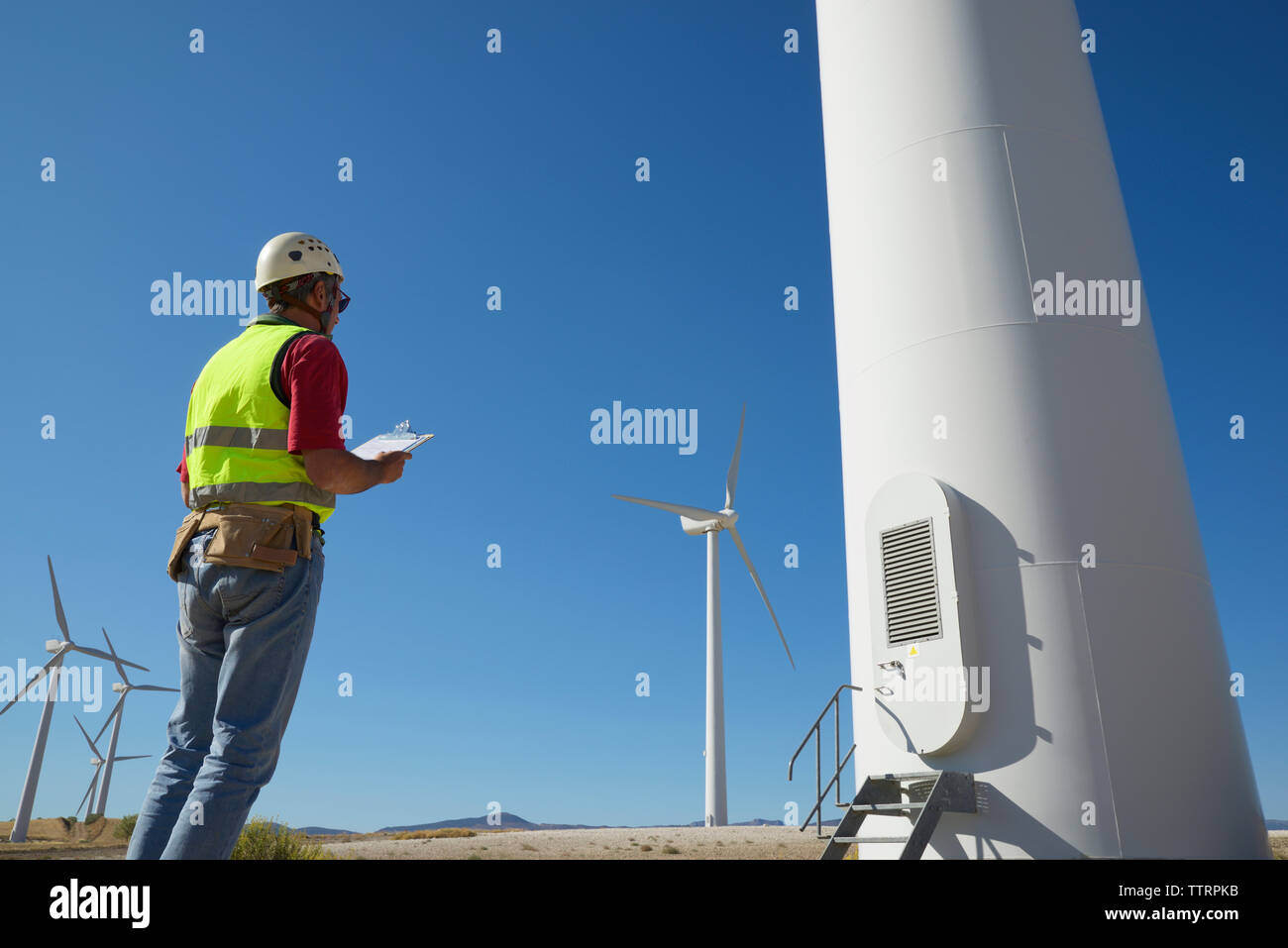Low Angle View von Ingenieur holding Zwischenablage beim Stehen mit Windmühlen gegen den Himmel Stockfoto