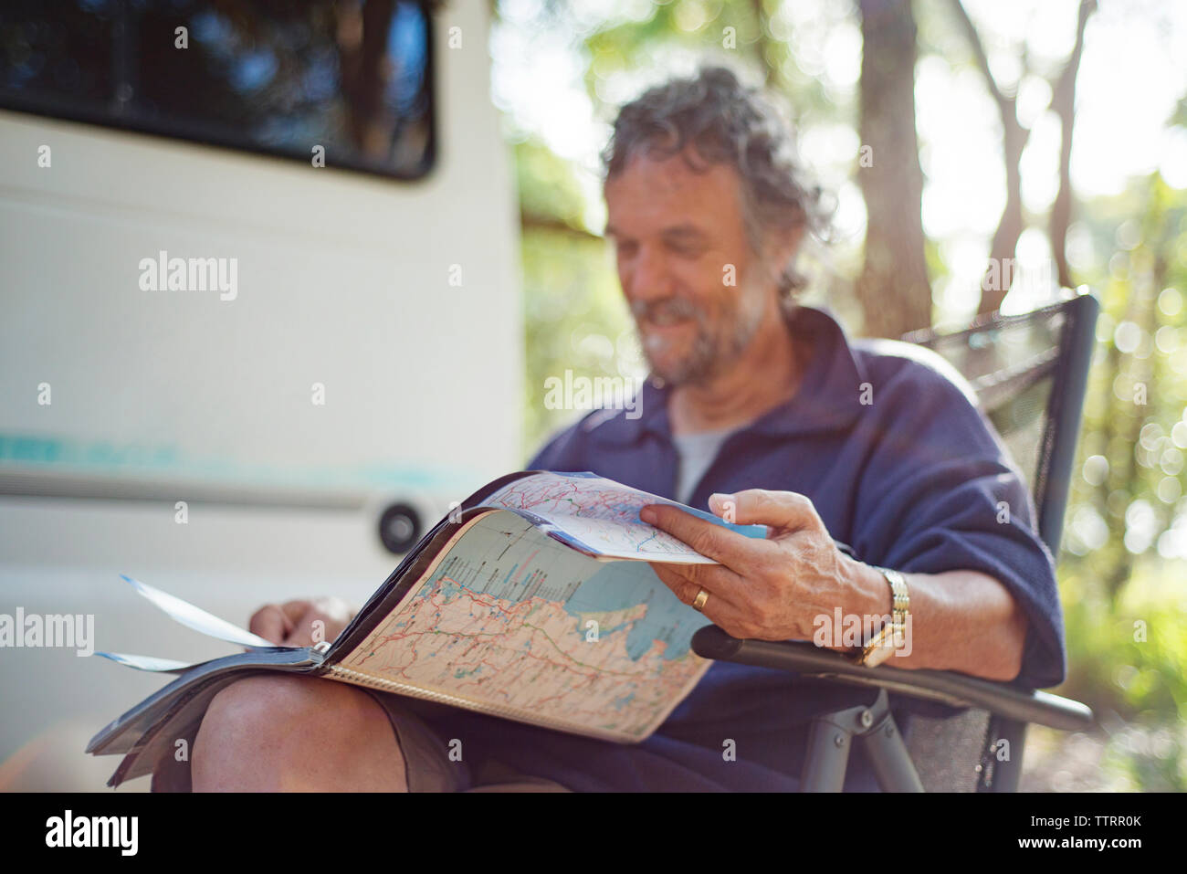 Gerne älterer Mann lesen Karte buchen Sie beim Sitzen auf Stuhl im Wald Stockfoto