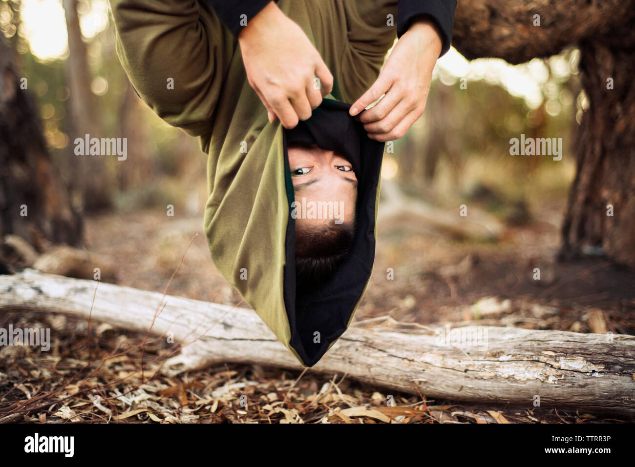 Porträt der Frau in der kapuzenjacke hängend kopfüber vom Baum Stockfoto