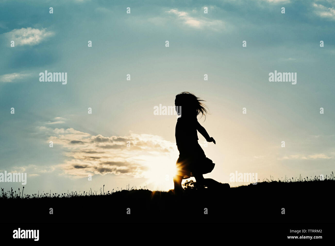 Silhouette Mädchen gehen auf Feld gegen Himmel bei Sonnenuntergang Stockfoto