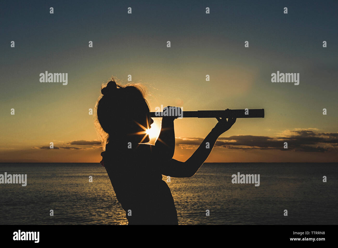 Silhouette Mädchen mit Teleskop gegen Meer bei Sonnenuntergang Stockfoto