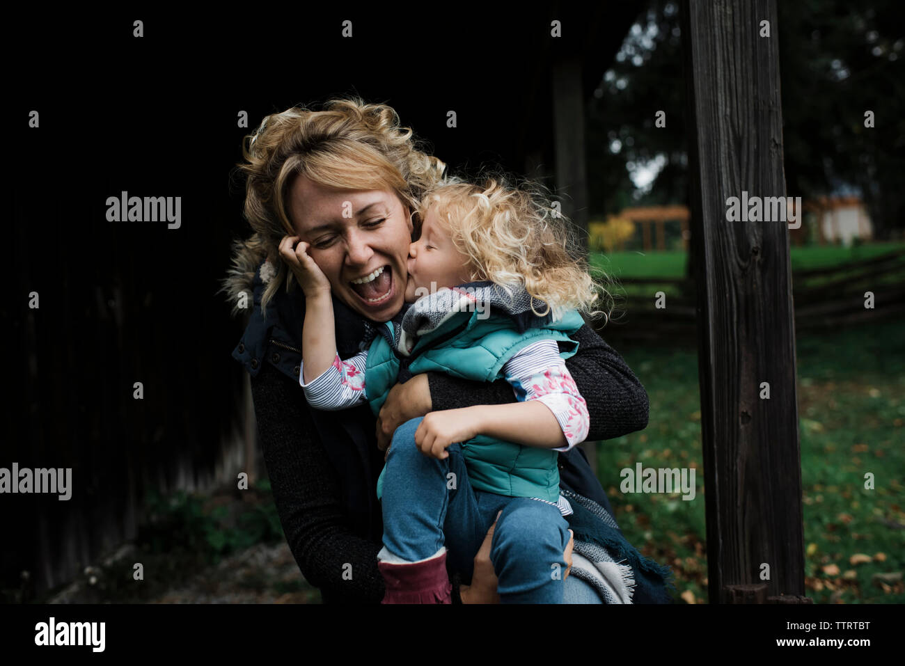 Tochter küssen fröhliche Mutter am Bauernhof Stockfoto