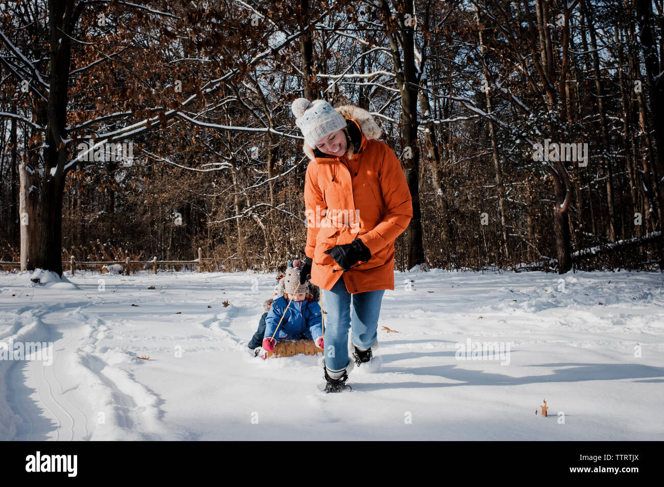 Glückliche Mutter ziehen Kinder auf Schlitten sitzen im Wald im Winter Stockfoto