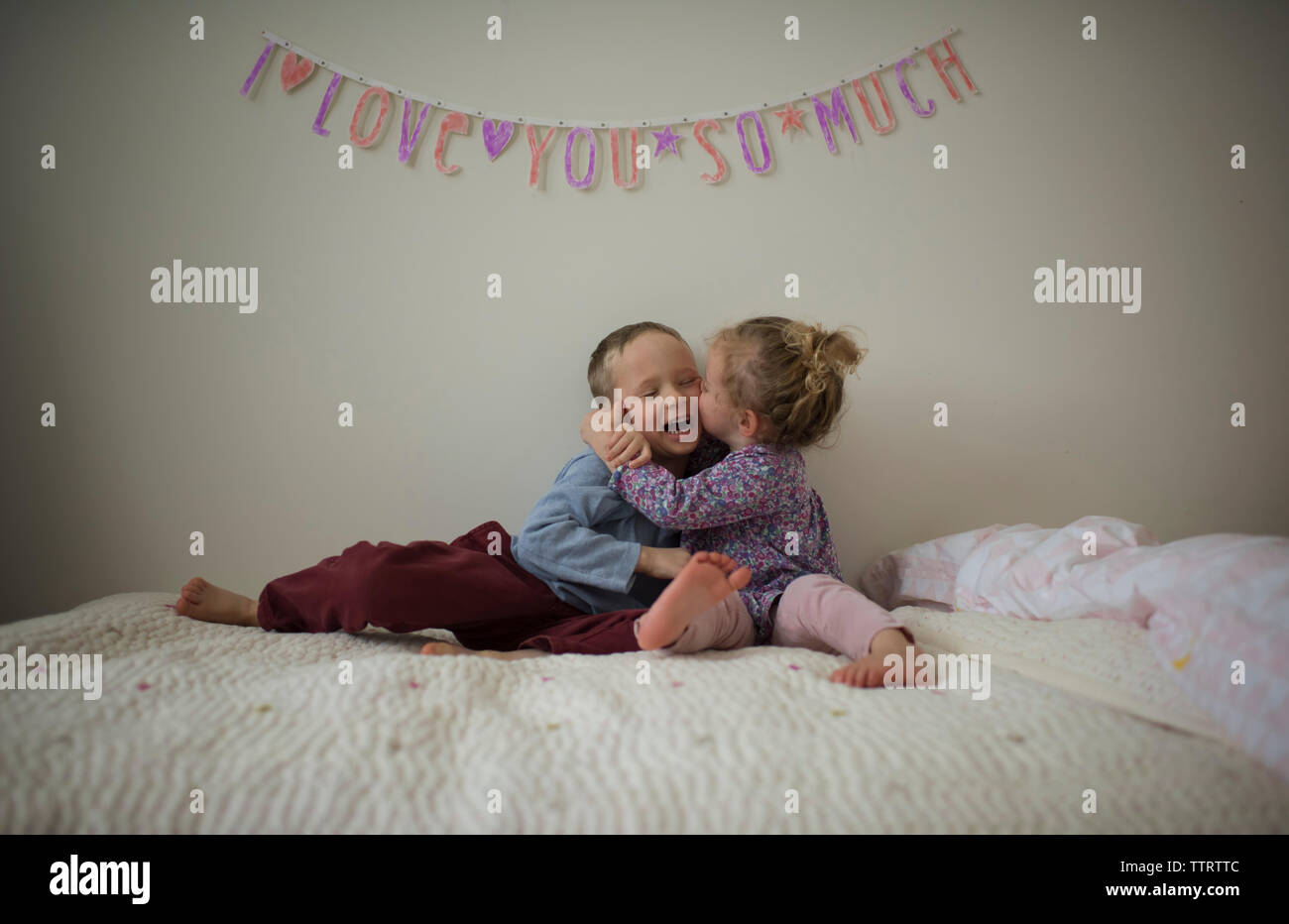 Glückliche Schwester küssen Bruder, während auf dem Bett zu Hause sitzen Stockfoto