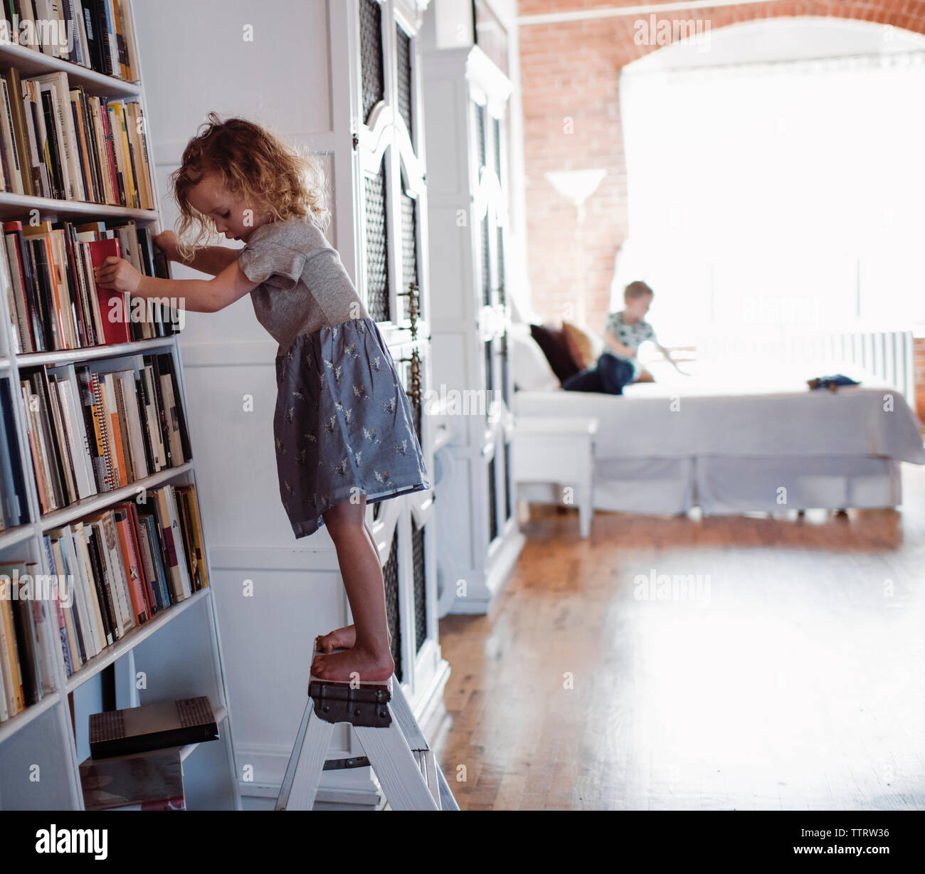 Seitliche Sicht auf Mädchen stehen Bücherregale Leiter mit Bruder im Hintergrund zu Hause Stockfoto