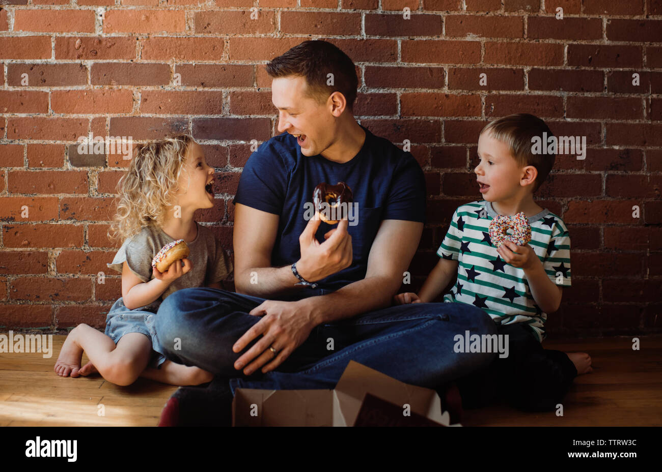 Gerne Vater mit Kindern essen Donuts, während auf dem Boden zu Hause sitzen Stockfoto