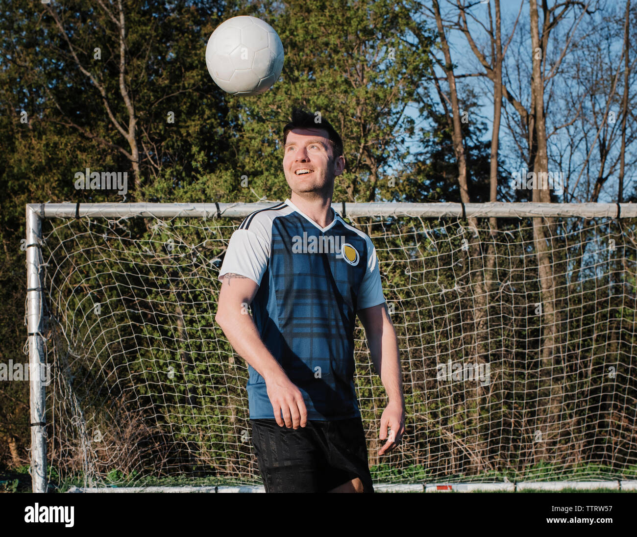 Glückliche Menschen spielen mit Fußball gegen Bäume im Park Stockfoto