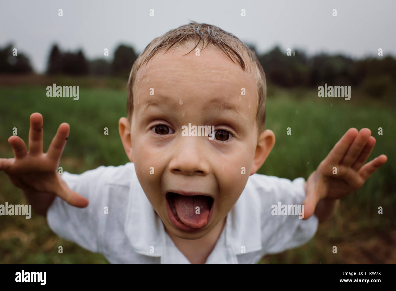 Portrait von wet Boy schreien beim Stehen gegen Himmel im Park während der Regenzeit Stockfoto