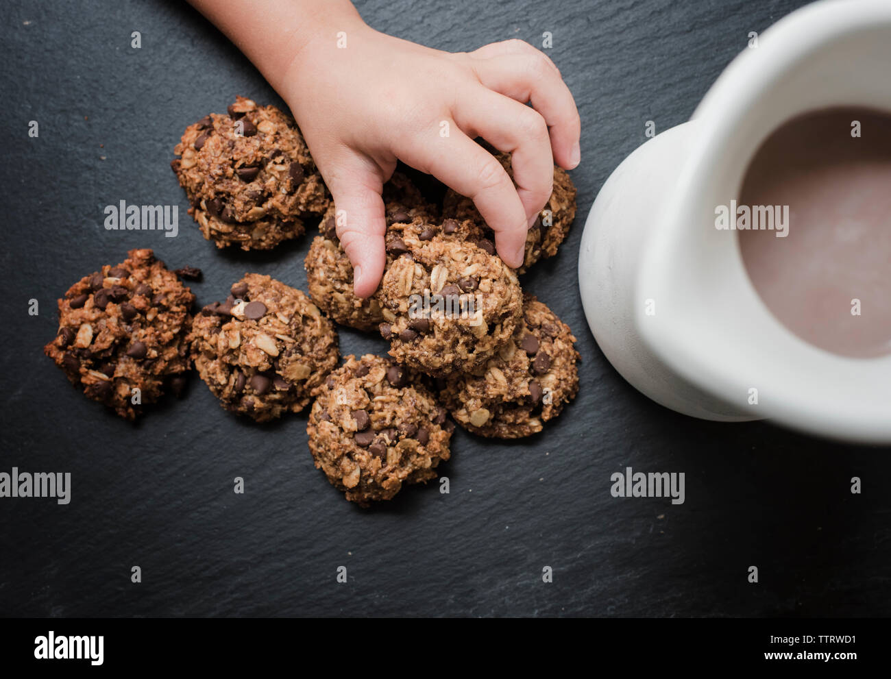 7/8 Hand des Mädchens Kommissionierung Chocolate Chip Cookies von Schiefer von Kaffee in der Kanne Stockfoto