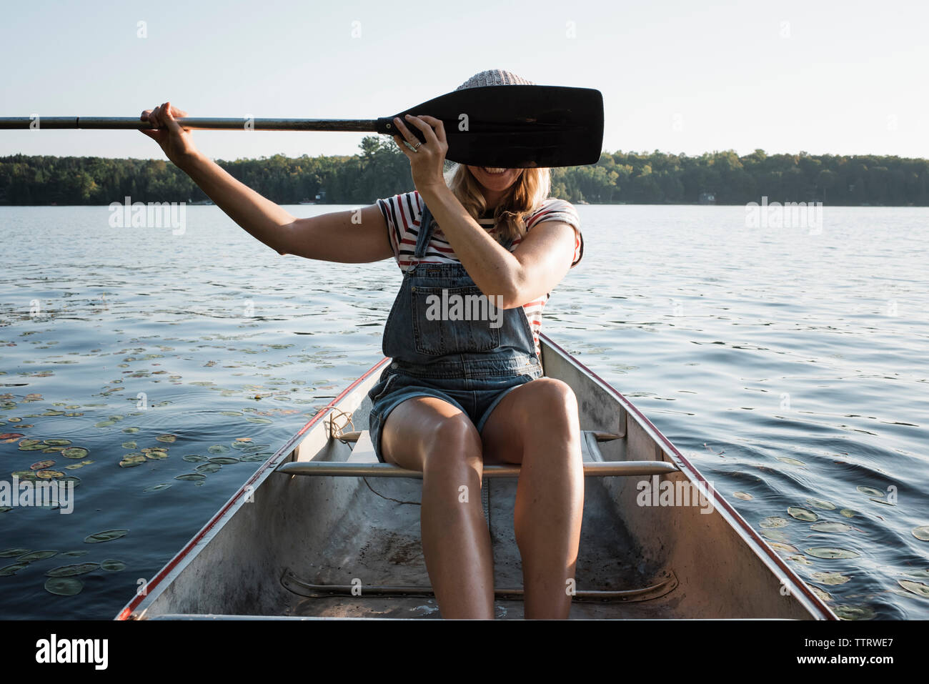 Glückliche Frau verstecken Gesicht mit Ruder beim Sitzen im Boot auf dem See gegen den Himmel in der Algonquin Provincial Park Stockfoto