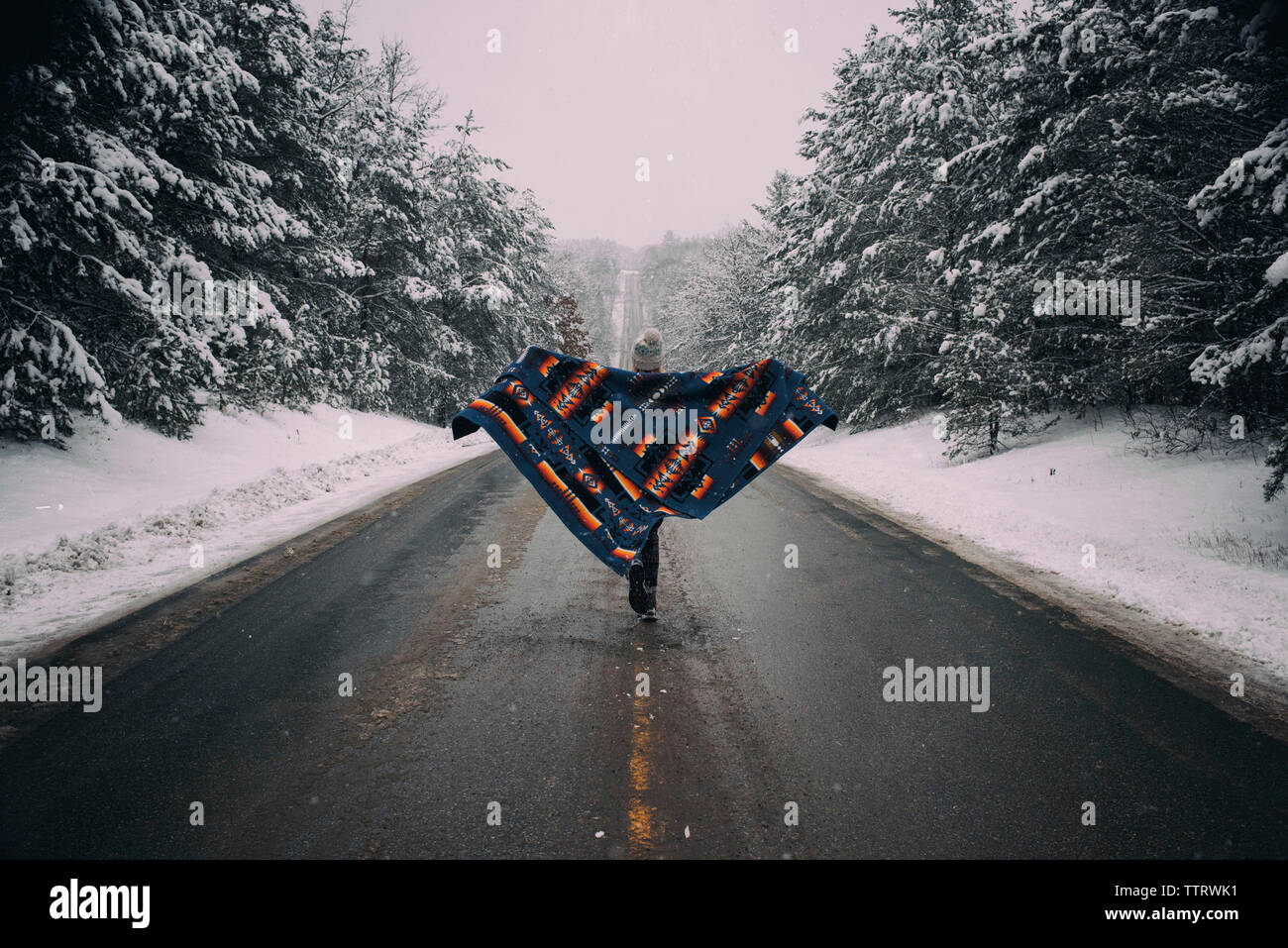 Ansicht der Rückseite Frau mit Decke zu Fuß auf der Straße inmitten einer schneebedeckten Bäumen im Wald Stockfoto