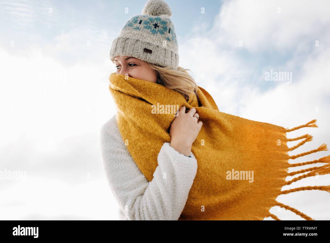 Blonde Frau hinter Schal am Strand lachend im Winter Stockfoto