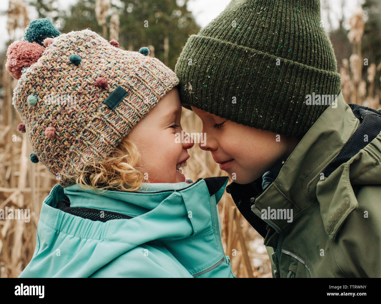 Bruder und Schwester berühren Köpfe spielen und lächelnd im Winter Stockfoto