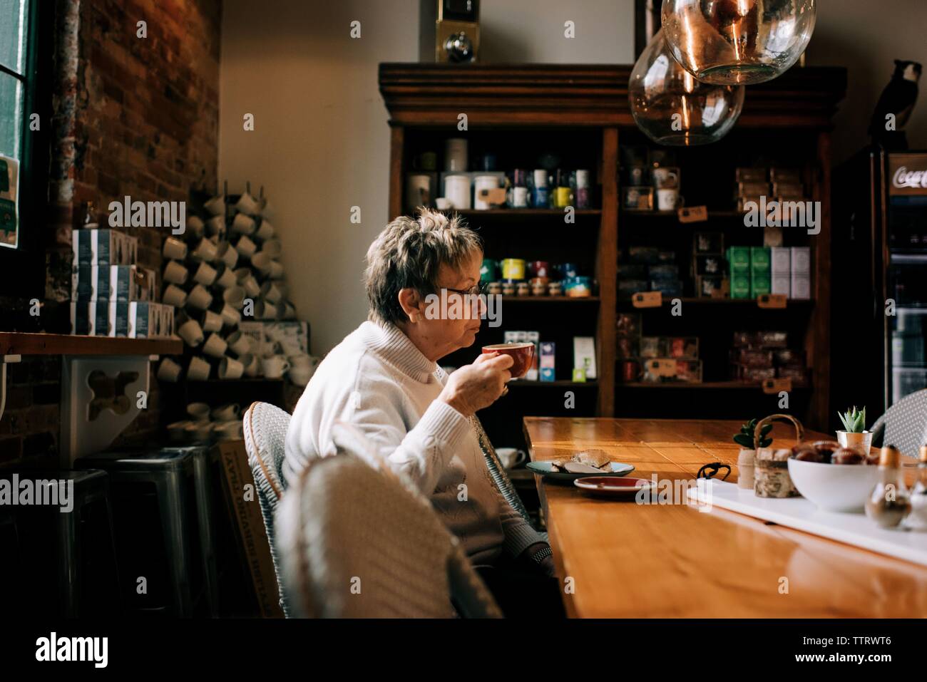 Ältere Frau trinkt Kaffee und Essen Bagel in einem Cafe Stockfoto