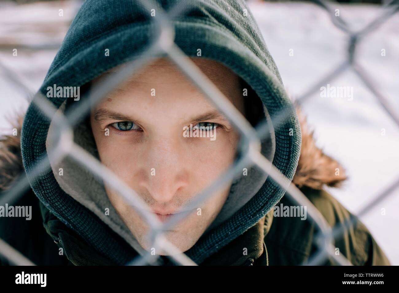 Porträt eines Mannes durch einen Zaun in die Kamera schaut im Winter Stockfoto