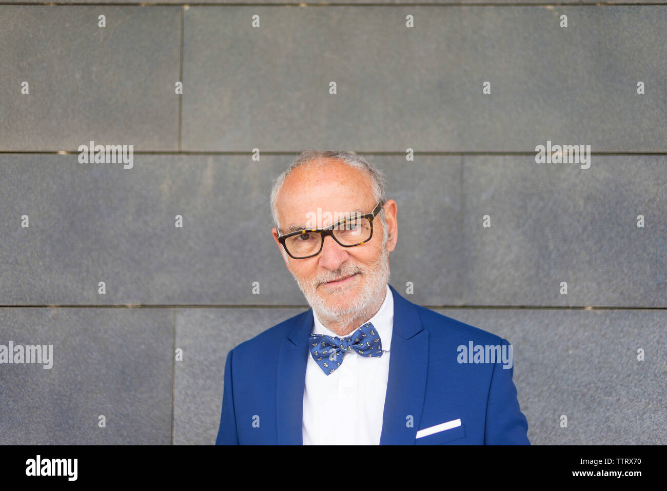 Portrait von zuversichtlich älterer Mann im Anzug gegen graue Wand stehend Stockfoto