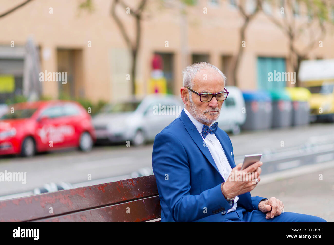 Zuversichtlich, dass ältere Menschen bei der Verwendung von Smart Phone, während auf der Bank gegen Gebäude Anzug Stockfoto