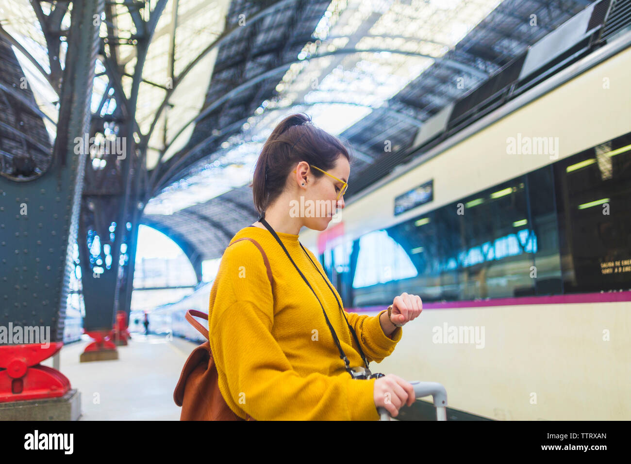 Seitenansicht der Frau mit Gepäck Kontrolle Zeit beim Stehen am Bahnhof Plattform Stockfoto