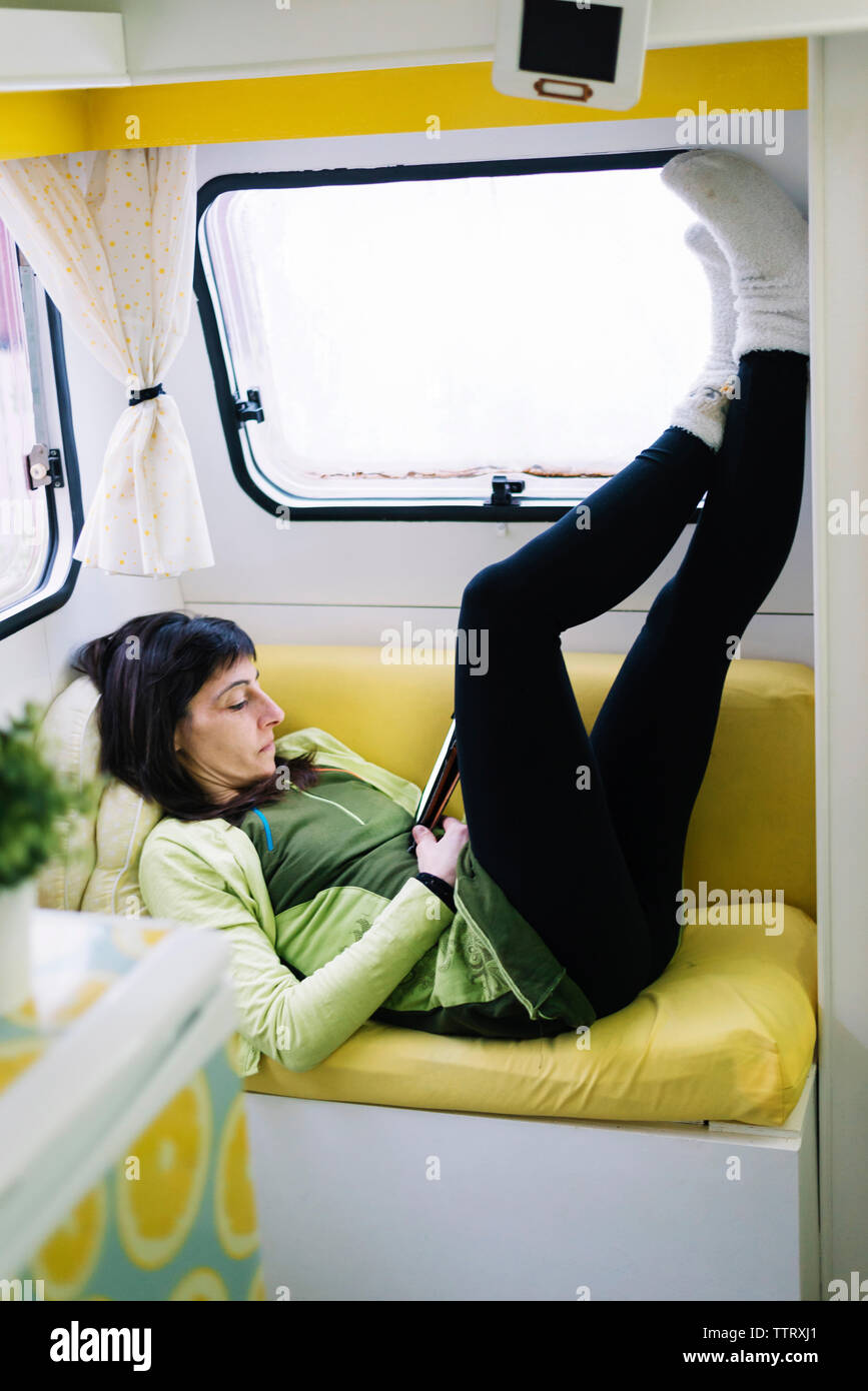Seitenansicht des liegende Frau auf dem Sofa lesen ebook, Beine wand Stockfoto