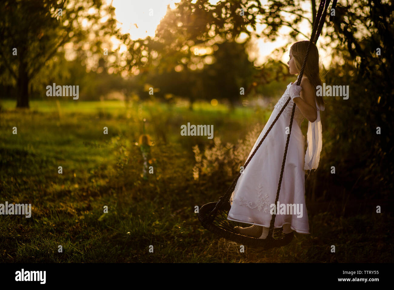 Seitliche Sicht auf Mädchen im Kleid schwingend auf Park bei Sonnenuntergang Stockfoto