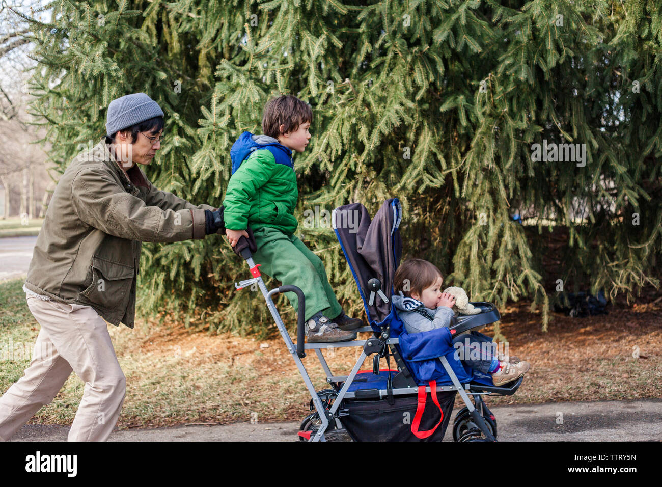 Seitenansicht des Vaters drücken Kinder sitzen auf Baby Stroller im Park Stockfoto