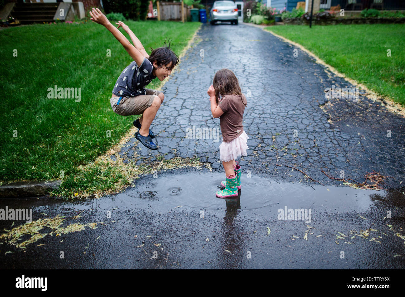 Seitenansicht des verspielten Geschwistern genießen auf nasser Straße während der Regenzeit Stockfoto