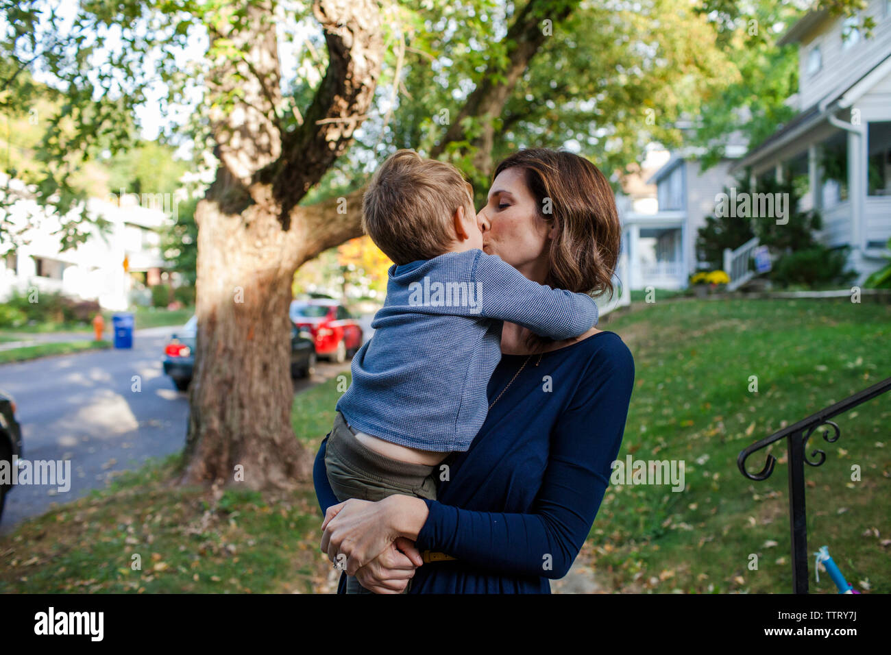 Mutter küssen Sohn beim Stehen gegen Bäume Stockfoto