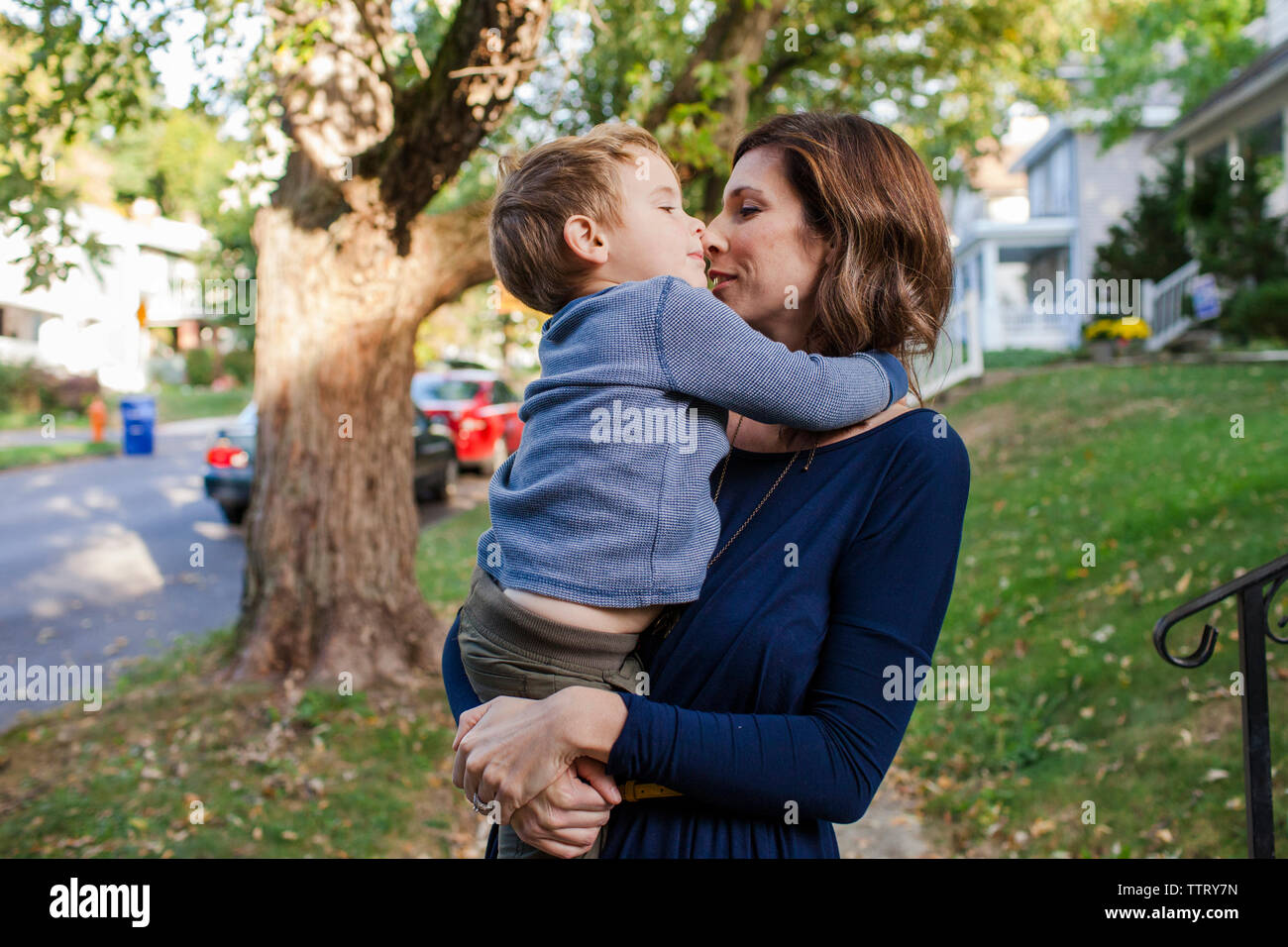 Mutter küssen niedlichen Sohn beim Stehen gegen Bäume Stockfoto