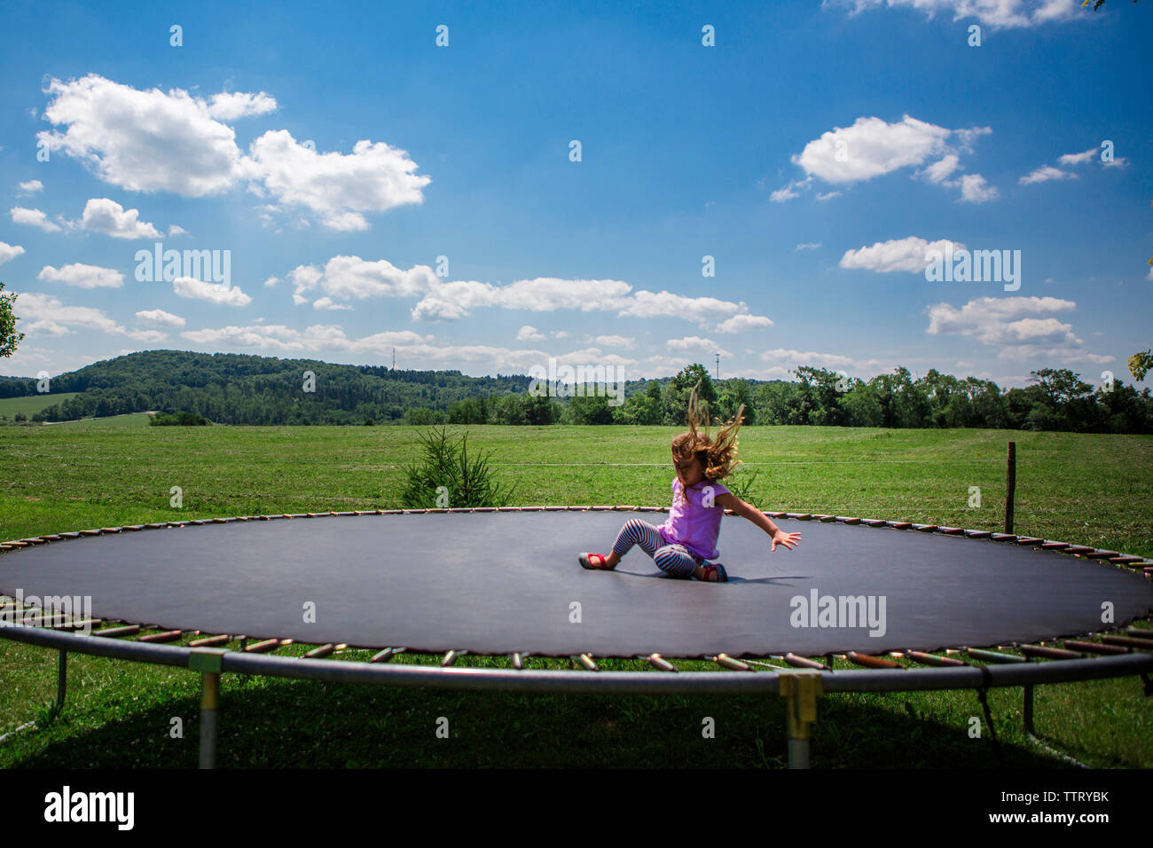 Verspielte Mädchen springen auf Trampolin gegen den blauen Himmel im Park während der sonnigen Tag Stockfoto