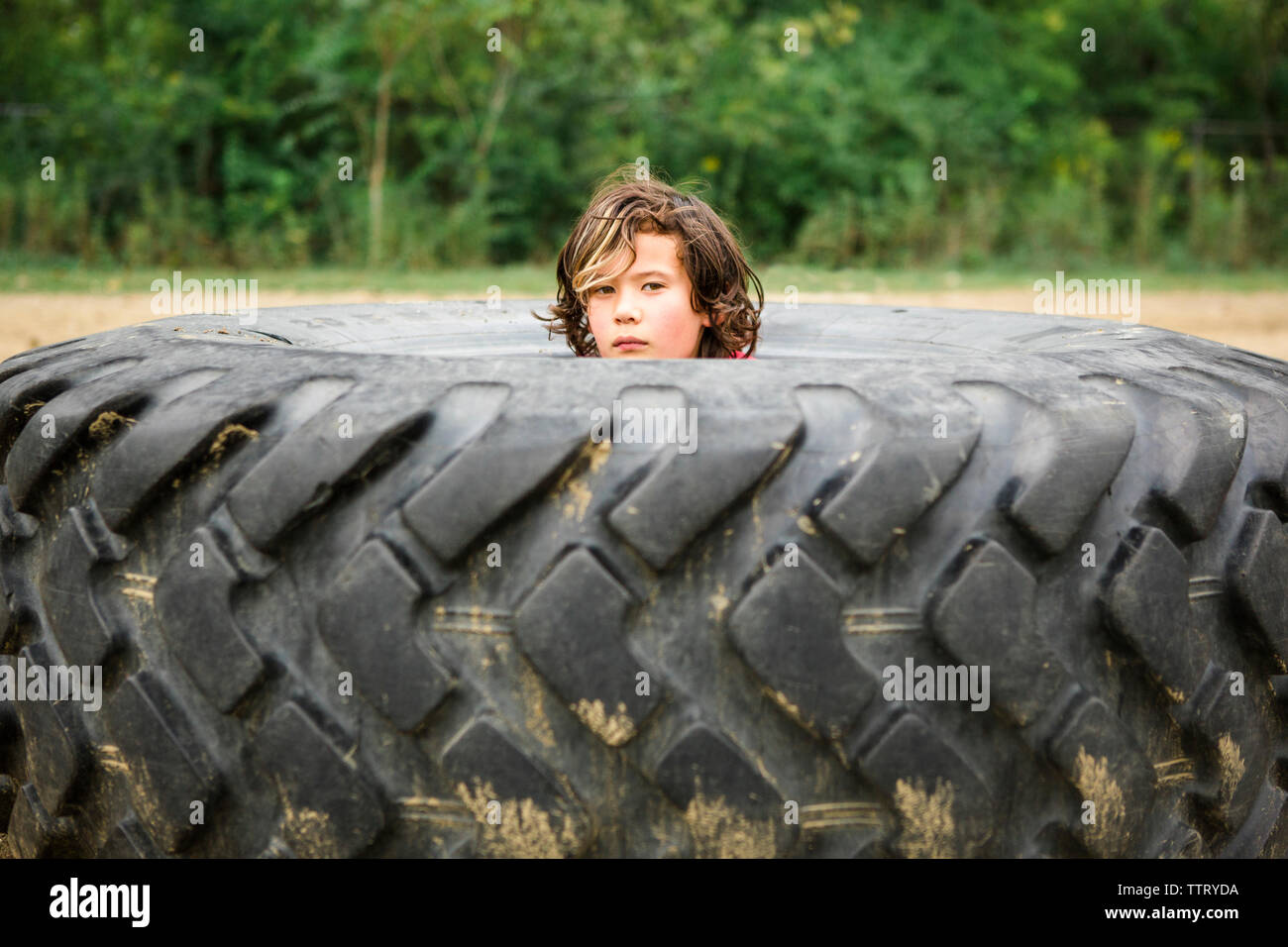 Portrait von cute Boy spähen durch schmutzige Reifen gegen Pflanzen Stockfoto