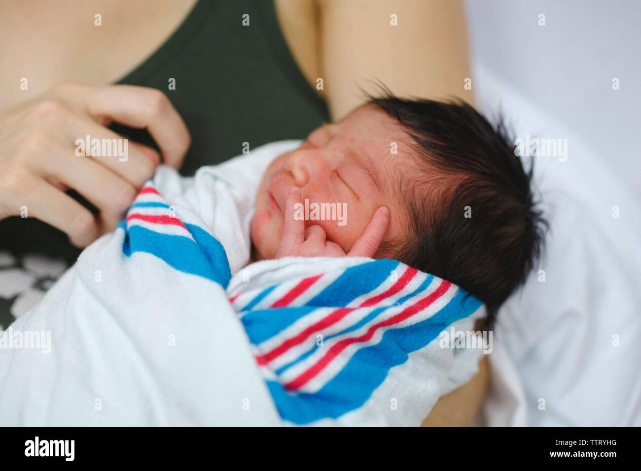 Ein neugeborenes Mädchen in eine Decke gehüllt, ruht in den Armen ihrer Mutter Stockfoto