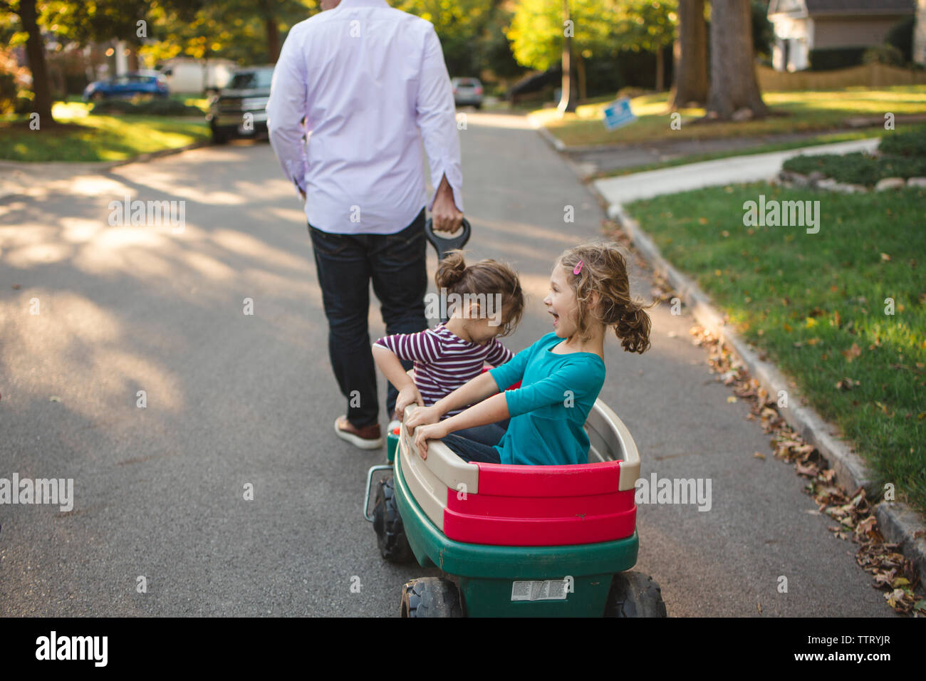 Ein Vater zieht seine glücklichen kleinen Mädchen auf der Straße in einem Wagen Stockfoto