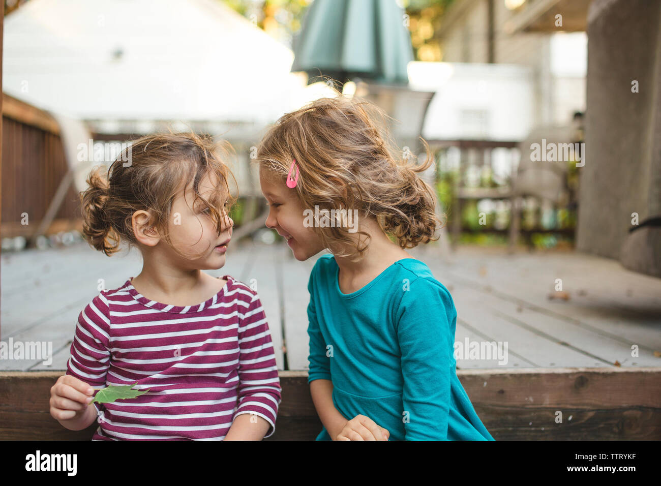 Zwei glückliche kleine Mädchen sitzen dicht zusammen, Draußen, Reden Stockfoto