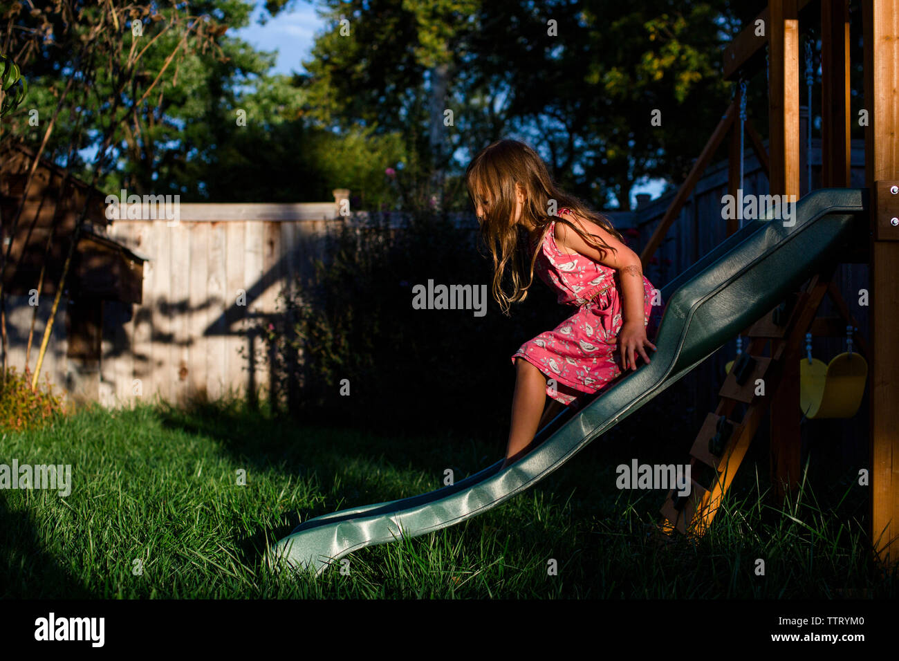 Ein kleines Mädchen Objektträger auf eine spielplatzgeräte in Ihrem Hinterhof bei Sonnenuntergang. Stockfoto