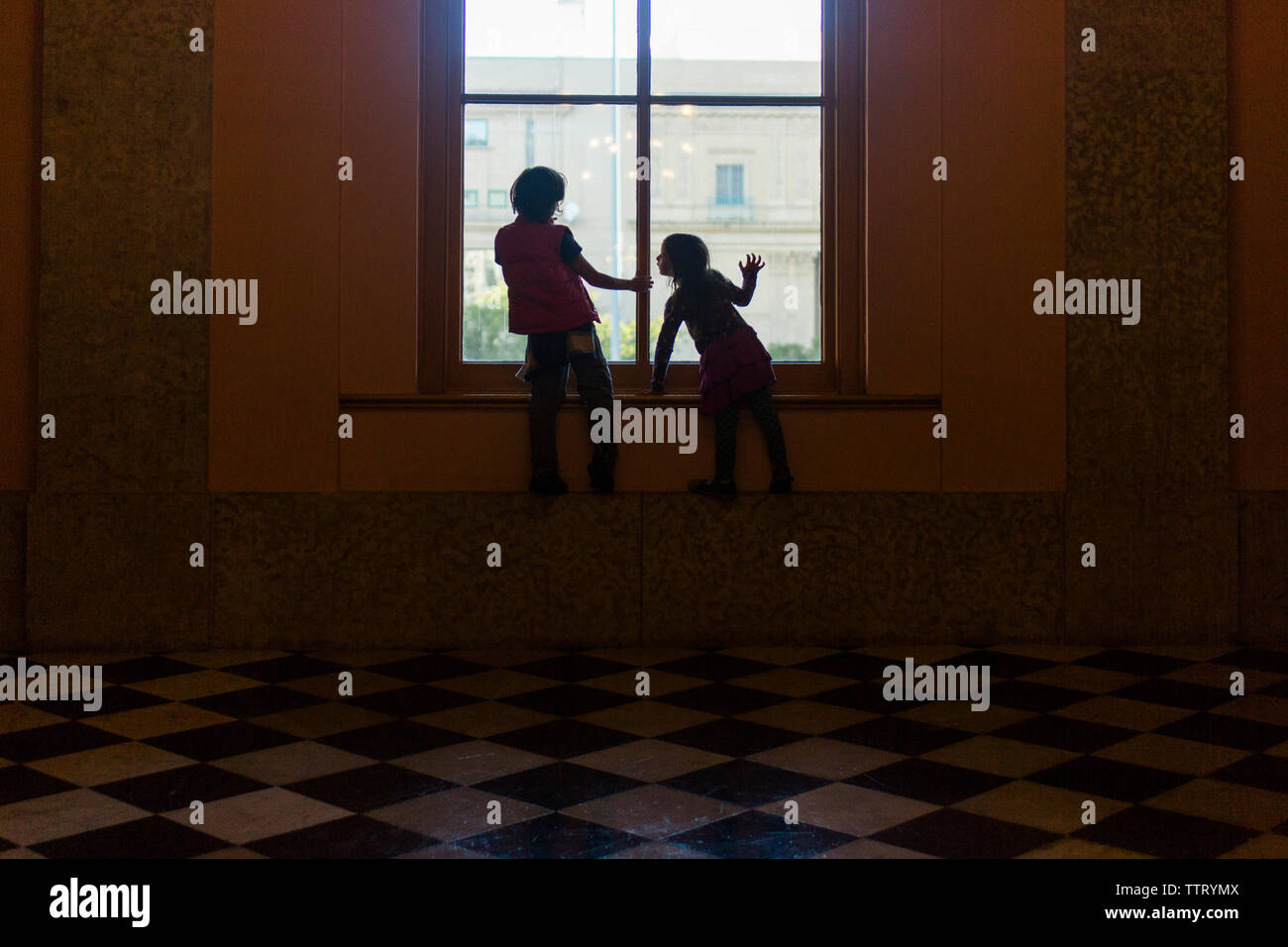 Zwei Kinder sind im Licht von einem großen Fenster silhoutted. Stockfoto