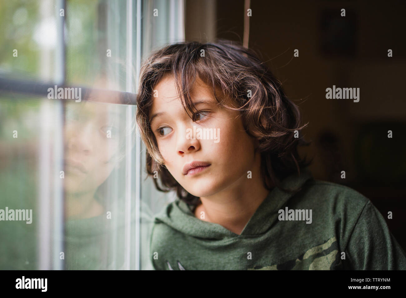 Ein Junge starrt aus dem Fenster mit ernsten Ausdruck auf seinem Gesicht Stockfoto