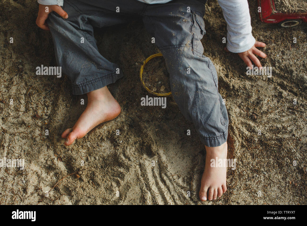 In der unteren Hälfte ein kleiner Junge spielt barfuß in einer Sandbox Stockfoto