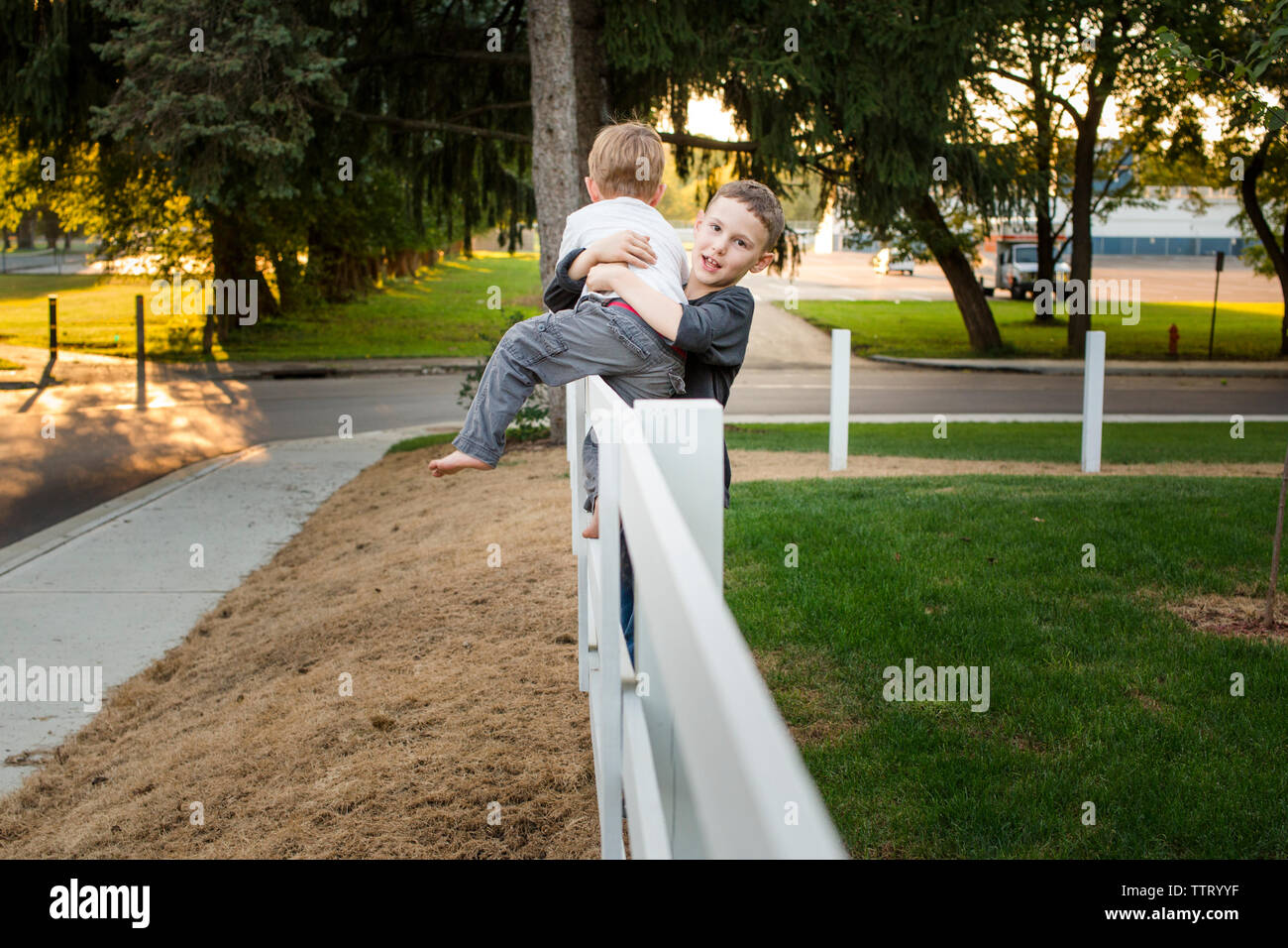 Ein Junge hilft seinem kleinen Bruder von einem Zaun erhalten Stockfoto