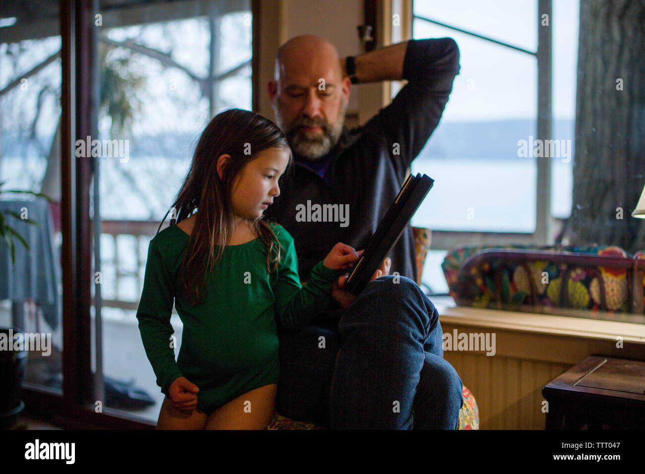 Ein kleines Mädchen in einem leotard schaut auf einen Tablet-PC mit ihrem Vater. Stockfoto