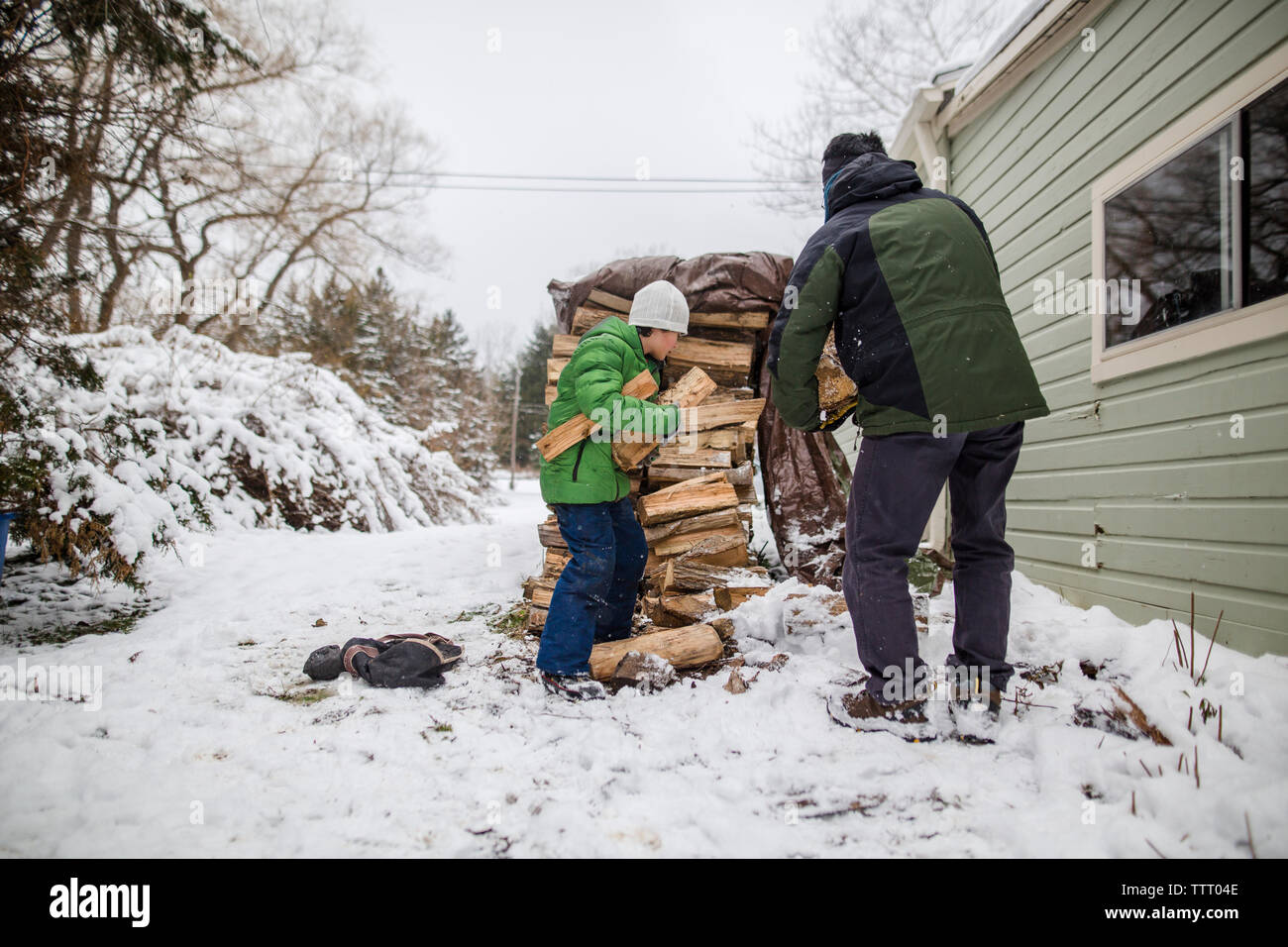 Ein kleiner Junge hilft seinem Vater Holz aus einem Wald Stack im Schnee sammeln Stockfoto