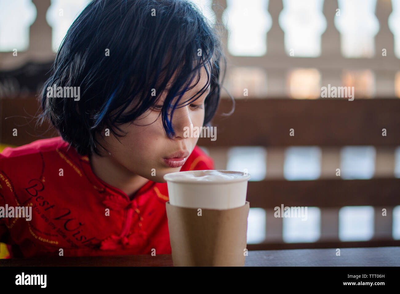 Die obere Hälfte der ein Junge das Blasen auf eine Tasse heiße Schokolade in ein Café im Freien Stockfoto