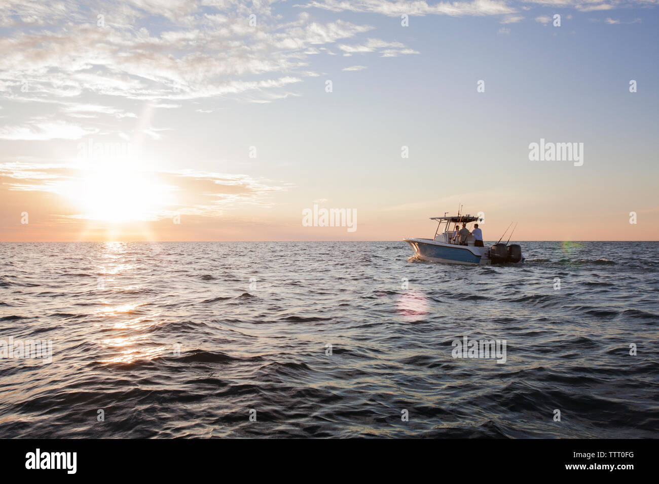 Männer und Jungen auf dem Boot auf dem Meer unterwegs gegen Himmel bei Sonnenuntergang Stockfoto