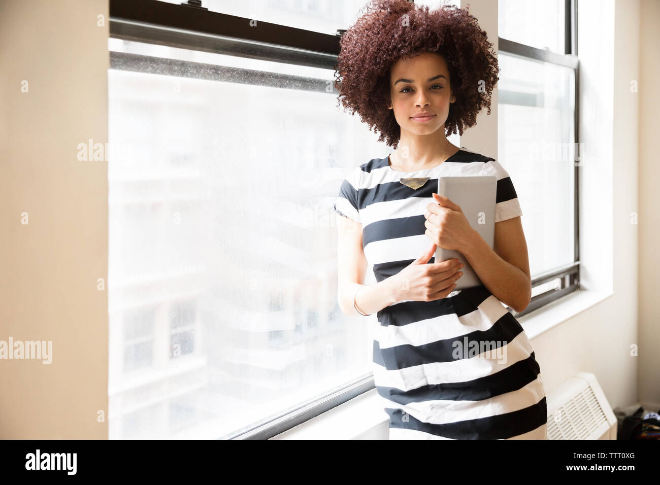 Portrait von zuversichtlich Geschäftsfrau holding Tablet Computer durch Fenster im Büro Stockfoto