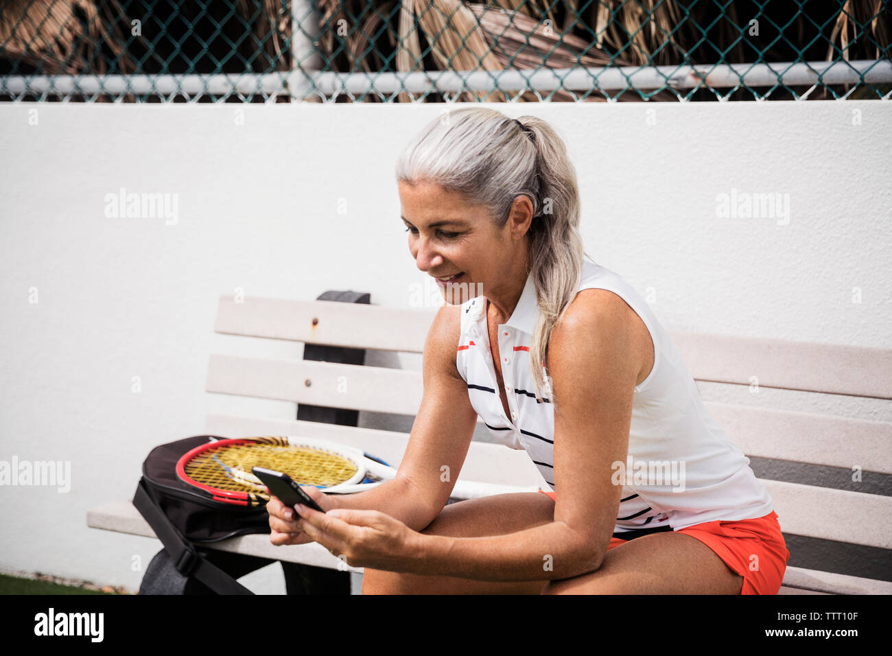 Reife Frau mit Smart Phone, während auf der Werkbank am Tennisplatz sitzen Stockfoto